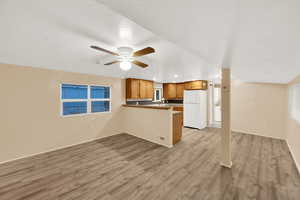 Kitchen with open floor plan, light wood-type flooring, freestanding refrigerator, brown cabinets, and recessed lighting