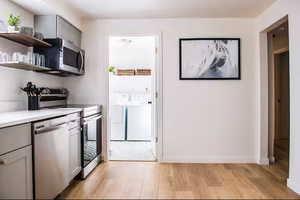 Kitchen featuring gray cabinets, appliances with stainless steel finishes, light countertops, light wood-style flooring, and open shelves