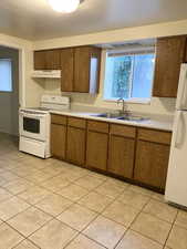 Kitchen featuring white appliances, brown cabinets, light countertops, under cabinet range hood, and light tile patterned floors