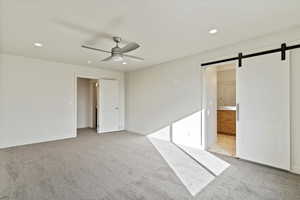 Master bedroom with a barn door, light carpet, recessed lighting, a ceiling fan, and ensuite bath