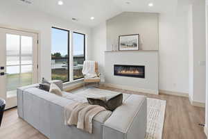 Living area featuring a glass covered fireplace, light wood-type flooring, recessed lighting, and lofted ceiling