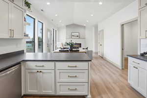 Kitchen featuring a peninsula, stainless steel dishwasher, white cabinets, open shelves, and dark countertops