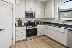 Kitchen with appliances with stainless steel finishes, light wood-style floors, hanging light fixtures, dark stone counters, and white cabinetry
