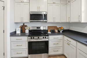 Kitchen featuring appliances with stainless steel finishes, dark countertops, and white cabinetry