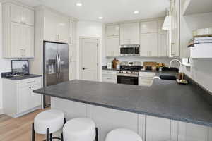Kitchen with a peninsula, dark countertops, appliances with stainless steel finishes, white cabinetry, and recessed lighting