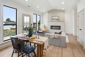 Dining space with a glass covered fireplace, light wood finished floors, recessed lighting, and vaulted ceiling