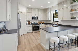 Kitchen featuring open shelves, a peninsula, appliances with stainless steel finishes, a breakfast bar, and pendant lighting