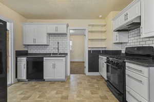Kitchen featuring decorative backsplash, black appliances, white cabinets, under cabinet range hood, and a textured ceiling