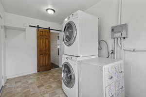Washroom with stacked washing machine and dryer, electric panel, a barn door, and stone finish flooring