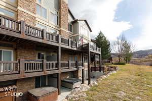 Back of house with stone siding, a yard, a patio, and a balcony