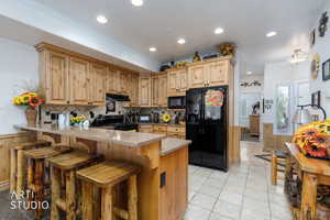 Kitchen featuring black appliances, a peninsula, a breakfast bar area, decorative backsplash, and a wainscoted wall