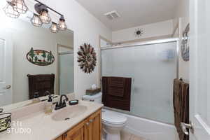 Bathroom featuring vanity, combined bath / shower with glass door, and a textured ceiling