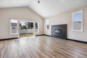 Unfurnished living room featuring light wood finished floors, a glass covered fireplace, high vaulted ceiling, recessed lighting, and a ceiling fan