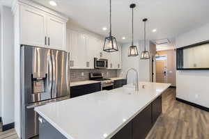 Kitchen featuring stainless steel appliances, dark wood finished floors, backsplash, decorative light fixtures, and white cabinetry