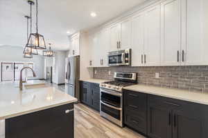 Kitchen featuring white cabinets, appliances with stainless steel finishes, dark cabinets, hanging light fixtures, and tasteful backsplash