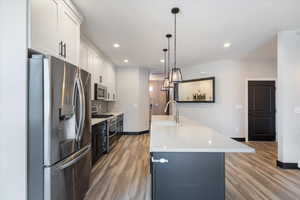 Kitchen featuring appliances with stainless steel finishes, white cabinetry, light wood-style flooring, pendant lighting, and recessed lighting