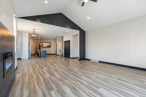 Unfurnished living room featuring light wood-style flooring, a chandelier, recessed lighting, high vaulted ceiling, and ceiling fan