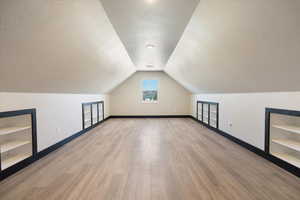 Bonus room with a textured ceiling, light wood-type flooring, vaulted ceiling, and built in features