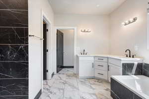 Bathroom featuring double vanity, light marble finish flooring, and a bath