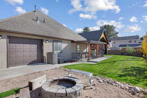 Back of house featuring a shingled roof, stucco siding, a patio area, an attached garage, and a fire pit