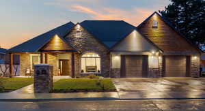 View of front of house with stone siding, driveway, roof with shingles, a yard, and a garage