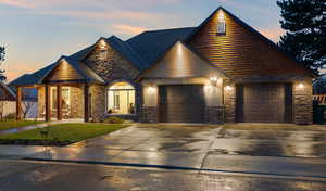 View of front of property featuring stone siding, concrete driveway, a front lawn, and a garage