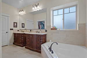 Full bathroom featuring a garden tub, a walk in closet, two vanities, and tile walls