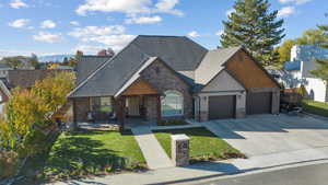 View of front of house featuring a front lawn, concrete driveway, a garage, stone siding, and a shingled roof