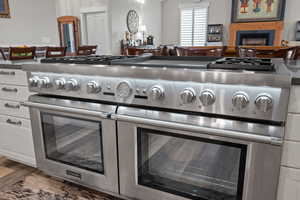 Detailed view of range with two ovens, a fireplace, white cabinetry, and dark stone countertops