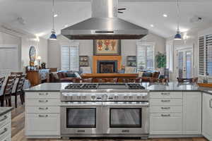 Kitchen with decorative light fixtures, 60 inch range hood, dark stone counters, range with two ovens (4 total in kitchen) , and white cabinetry