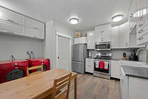 Kitchen featuring dark countertops, stainless steel appliances, white cabinets, light wood-style floors, and washer / clothes dryer