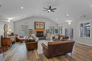 Living room featuring dark wood-type flooring, french doors, vaulted ceiling, a fireplace with raised hearth, and ceiling fan