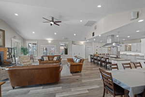 Living area with recessed lighting, light wood-type flooring, a fireplace, ceiling fan, and high vaulted ceiling