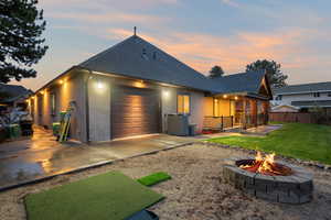 Back of property at dusk featuring roof with shingles, stucco siding, driveway, a patio area, and a garage