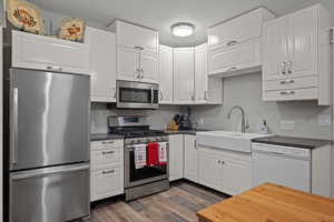 Full Kitchen with stainless steel appliances, dark LVP flooring, white cabinetry, and dark stone countertops