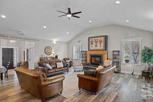 Gathering Room!  Living area with lofted ceiling, wood finished floors, a fireplace with raised hearth, recessed lighting, and ceiling fan