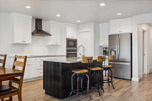 Kitchen featuring appliances with stainless steel finishes, white cabinets, wall chimney exhaust hood, tasteful backsplash, and recessed lighting