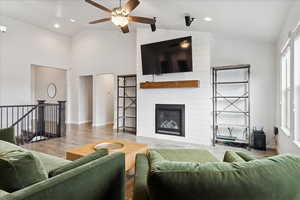 Living room featuring wood finished floors, a fireplace, lofted ceiling, ceiling fan, and recessed lighting