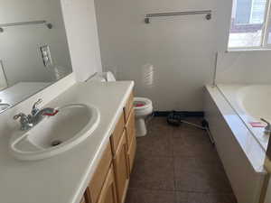 Full bathroom featuring a garden tub, vanity, and dark tile patterned flooring