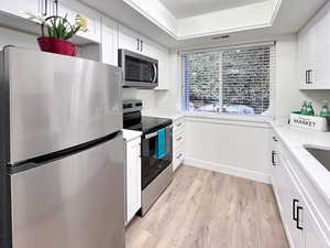 Beautifully renovated kitchen with stainless steel appliances, new white cabinets, light wood finished floors, artistic style ceiling, and light stone counters