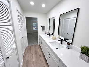 Primary full bathroom with double vanity, multiple closets, light wood-style floors, and warm, recessed lighting