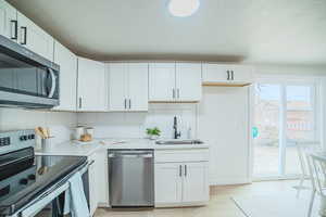 Kitchen with stainless steel appliances, white cabinetry, tasteful backsplash, light stone counters, and a textured ceiling