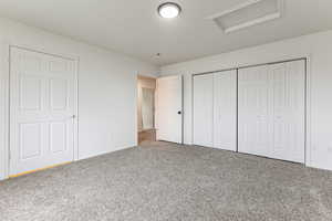 Unfurnished bedroom featuring attic access, carpet flooring, a closet, and a textured ceiling