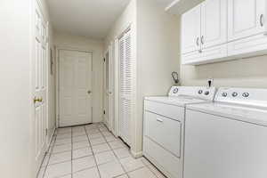 Laundry area with light tile patterned floors, washer and clothes dryer, cabinet space, and a textured ceiling