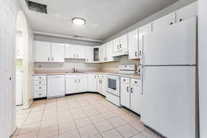 Kitchen featuring white appliances, light countertops, light tile patterned flooring, glass insert cabinets, and white cabinets