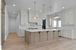Kitchen featuring light wood finished floors, large island, decorative light fixtures, breakfast bar, and recessed lighting