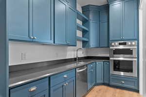 Butler pantry with open shelves, blue cabinetry, dark stone counters, light wood-style flooring, and stainless steel appliances