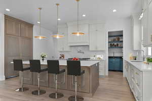 Kitchen featuring light stone counters, kitchen bar, decorative light fixtures, center island, and paneled built in refrigerator