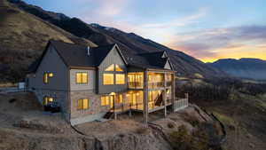 Back of house at dusk with pool, spa, copper rain gutters, stone siding, board and batten siding, decks with valley and mountain views, and stairway between decks