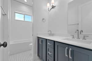 Full bath featuring double vanity and light tile patterned floors, between main level bedrooms